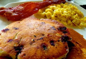 Blueberry pancakes, scrambled eggs, and crispy bacon.
